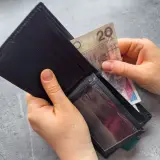 Dłonie wkładają banknot 20 zł do czarnego portfela. Zastanawiasz się, po jakim czasie od zarejestrowania wypłacany jest zasiłek dla bezrobotnych?