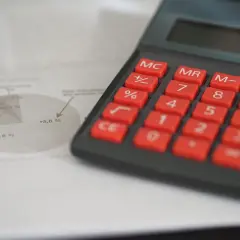 Kalkulator i wykres kołowy na papierze, pomagające analizować koszty rodzajowe i ich zmiany.