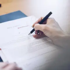 Dłoń podpisuje testament allograficzny. Dokument prawny, pióro i pieczęć na biurku.