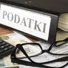 Segregator z napisem "PODATKI", okulary, kalkulator i pieniądze na dokumentach. Wszystko gotowe do rozliczenia rezydencji podatkowej.
