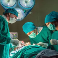 Trzech chirurgów w zielonych fartuchach i maseczkach skupionych na pacjencie. Zastanawiasz się, ile zarabia chirurg?
