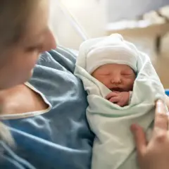 Matka tuli noworodka, który śpi otulony kocykiem. To piękny moment, który symbolizuje świadczenie rodzicielskie.