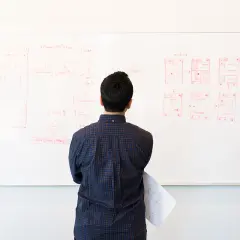 Mężczyzna analizuje schemat na tablicy, planując **restrukturyzację** projektu.