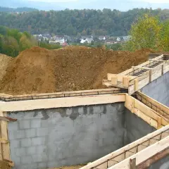 Fundamenty domu w budowie, zbrojenie i szalunki. Widać kopce ziemi i zabudowania w tle. Ważne jest pozwolenie na budowę, by wszystko szło zgodnie z planem.