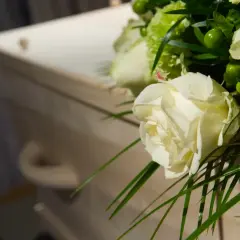Białe róże i zielone dodatki na drewnianej trumnie. Warto pamiętać o zasiłku pogrzebowym 6000 zł.