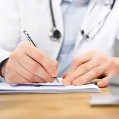 Lekarz w białym kitlu pisze na dokumentach. Zastanawiasz się nad ubezpieczeniem zdrowotnym bez pracy?