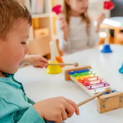 Chłopiec **aktywnie w żłobku** gra na cymbałkach, obok kolorowe dzwonki.