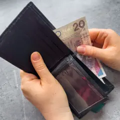 Dłonie wkładają banknot 20 zł do czarnego portfela. Zastanawiasz się, po jakim czasie od zarejestrowania wypłacany jest zasiłek dla bezrobotnych?
