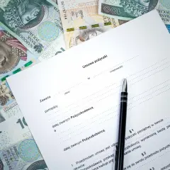 Umowa kredytowa z długopisem i polskimi banknotami. Dokument zawiera nagłówek "Umowa pożyczki" i pola do wypełnienia.