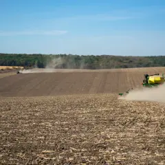 Traktor z siewnikiem na polu, wzbijający tumany kurzu.