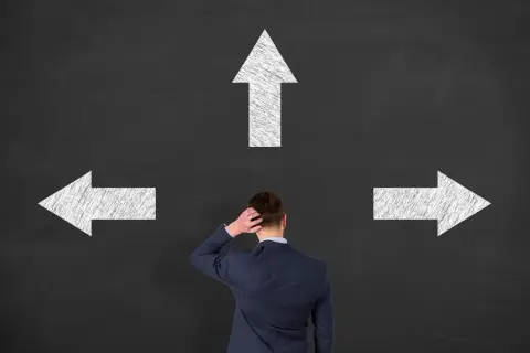 Biznesmen przed tablicą z trzema strzałkami. Dylemat wyboru ścieżki, kluczowy dla etyki w biznesie.