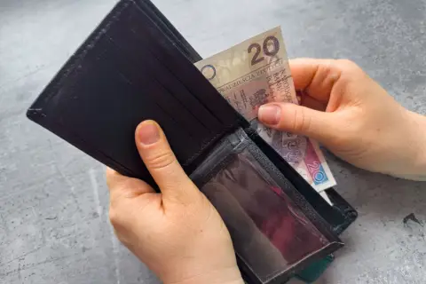 Dłonie wkładają banknot 20 zł do czarnego portfela. Zastanawiasz się, po jakim czasie od zarejestrowania wypłacany jest zasiłek dla bezrobotnych?