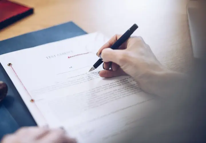 Dłoń podpisuje testament allograficzny. Dokument prawny, pióro i pieczęć na biurku.