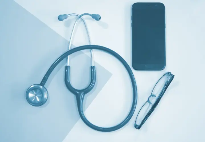 Stetoskop, okulary i telefon leżą obok siebie. To może być pomocne przy pytaniu, jak obliczyć dochód do składki zdrowotnej.