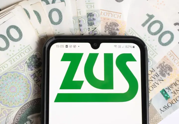 ZUS na ekranie telefonu, w tle polskie banknoty. Informacje o stopie procentowej składek na ubezpieczenie wypadkowe.