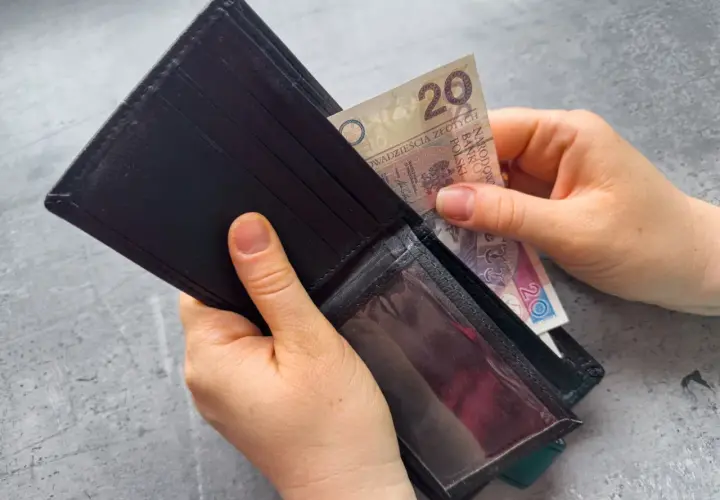 Dłonie wkładają banknot 20 zł do czarnego portfela. Zastanawiasz się, po jakim czasie od zarejestrowania wypłacany jest zasiłek dla bezrobotnych?