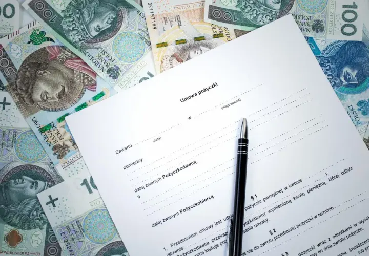 Umowa kredytowa z długopisem i polskimi banknotami. Dokument zawiera nagłówek "Umowa pożyczki" i pola do wypełnienia.