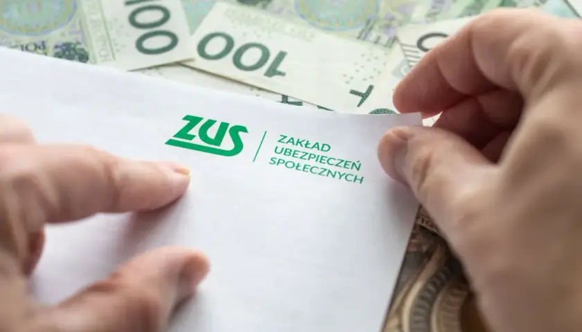 Dłonie trzymają dokument ZUS na tle banknotów 100 zł. Może to być związane z jednorazową wypłatą z subkonta ZUS.