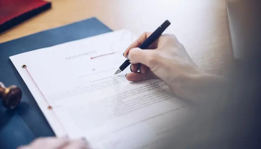 Dłoń podpisuje testament allograficzny. Dokument prawny, pióro i pieczęć na biurku.