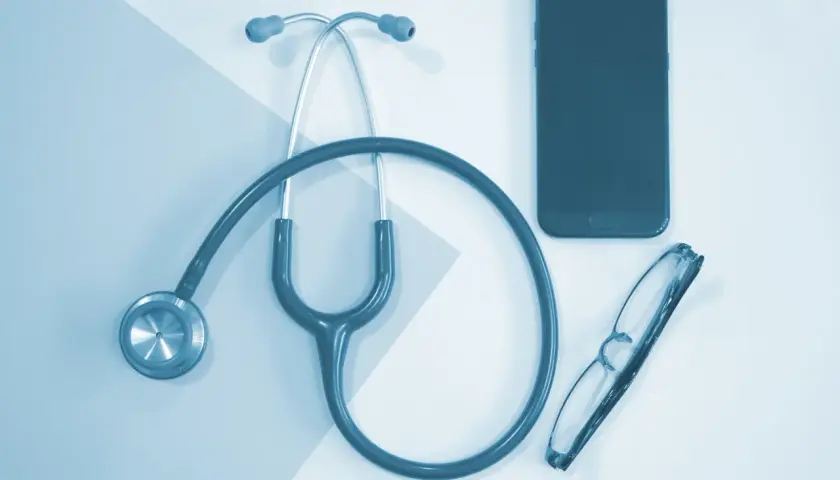 Stetoskop, okulary i telefon leżą obok siebie. To może być pomocne przy pytaniu, jak obliczyć dochód do składki zdrowotnej.