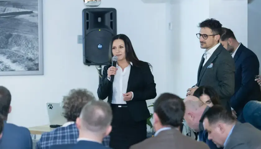 Kobieta w garniturze przemawia do grupy ludzi podczas spotkania.