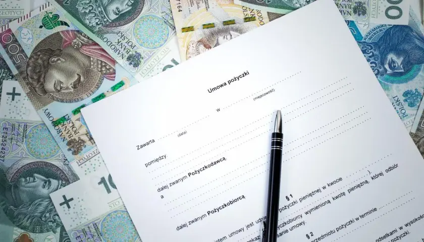 Umowa kredytowa z długopisem i polskimi banknotami. Dokument zawiera nagłówek "Umowa pożyczki" i pola do wypełnienia.