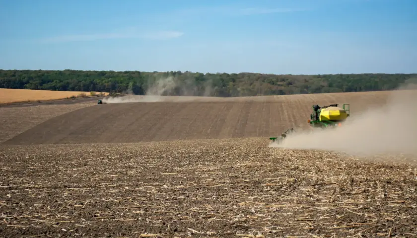Traktor z siewnikiem na polu, wzbijający tumany kurzu.