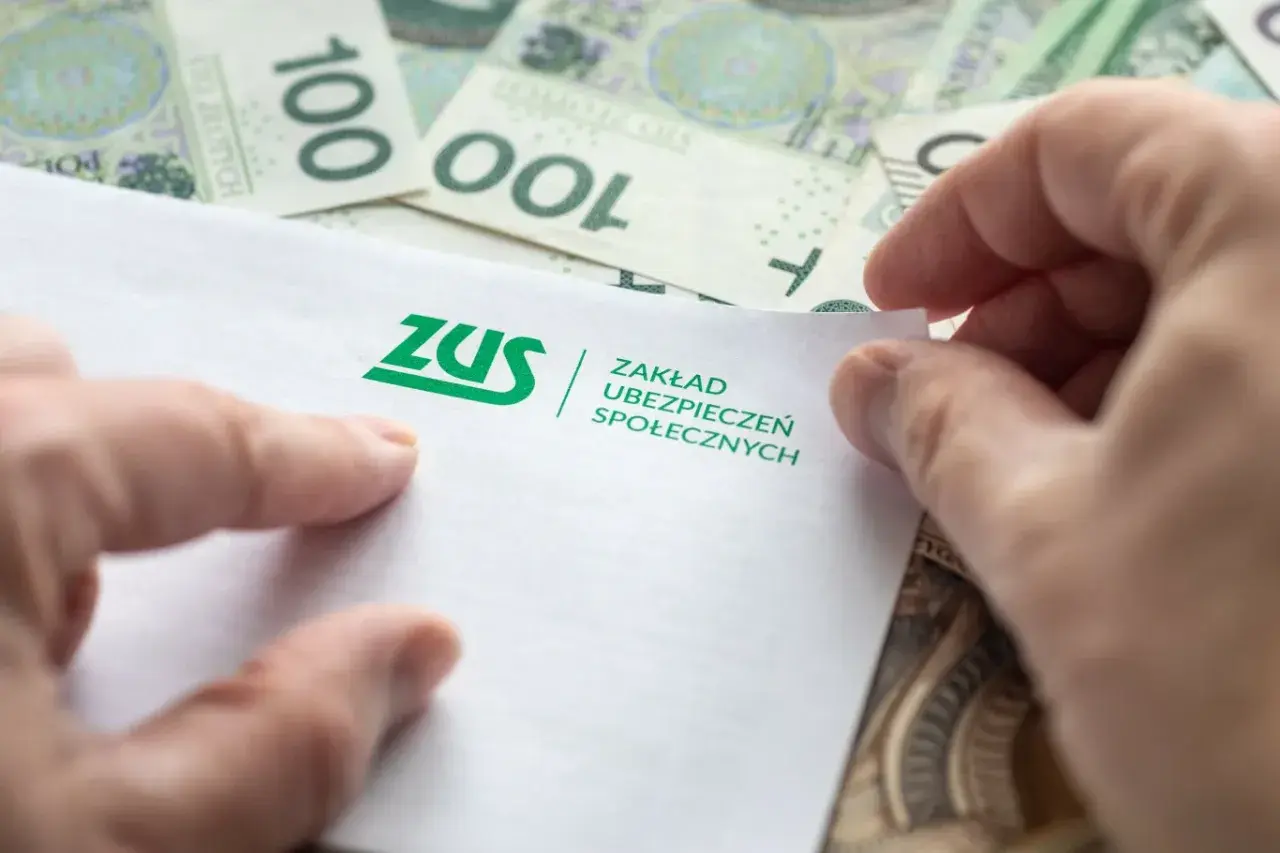 Dłonie trzymają dokument ZUS na tle banknotów 100 zł. Może to być związane z jednorazową wypłatą z subkonta ZUS.