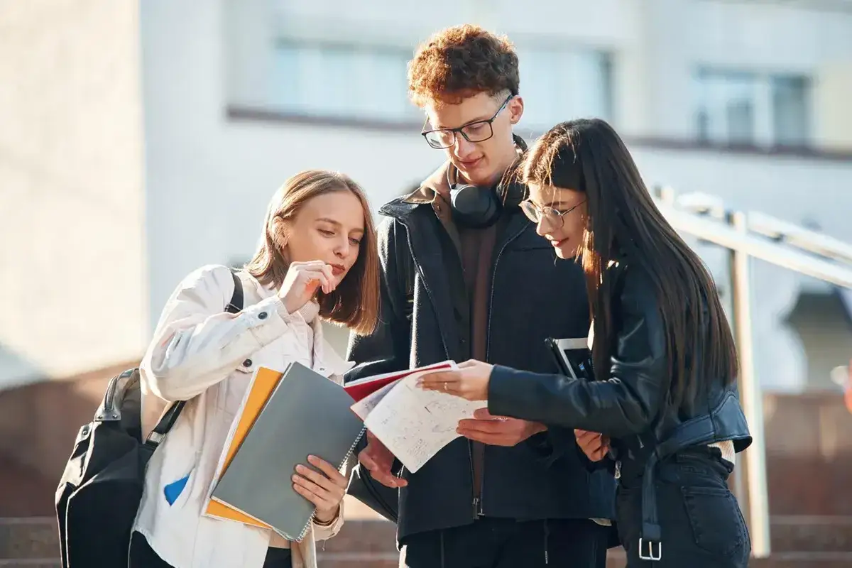 Trzech studentów dyskutuje nad notatkami, być może planując umowę zlecenie dla studenta.
